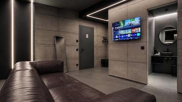 Eine moderne, minimalistische Lobby mit einer Ledersitzgruppe, einem digitalen Fernsehbildschirm und einem kleinen Badezimmer mit Spiegel und Waschbecken.