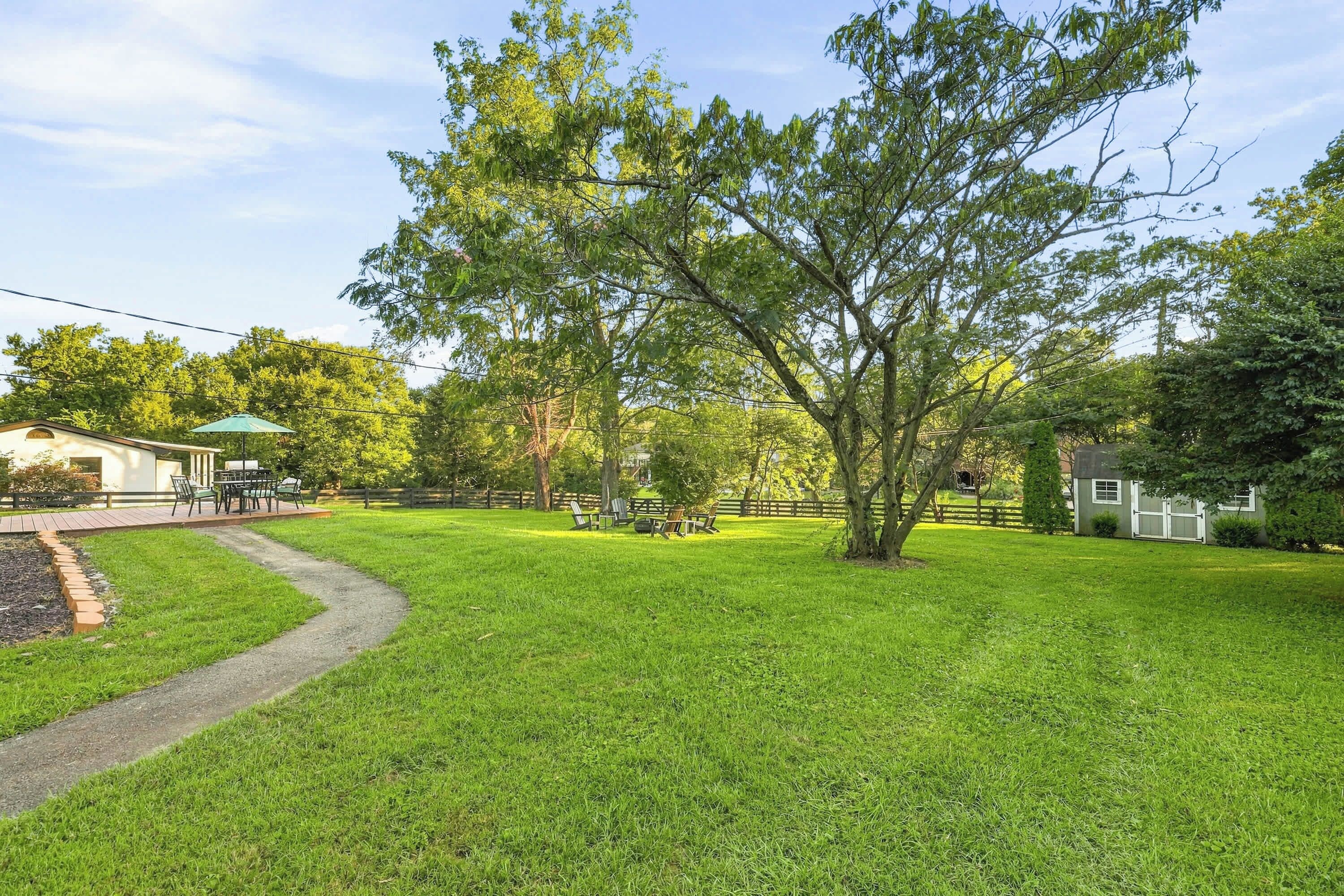A well-maintained lawn with a paved path, a picnic table, and a small building with a green roof.