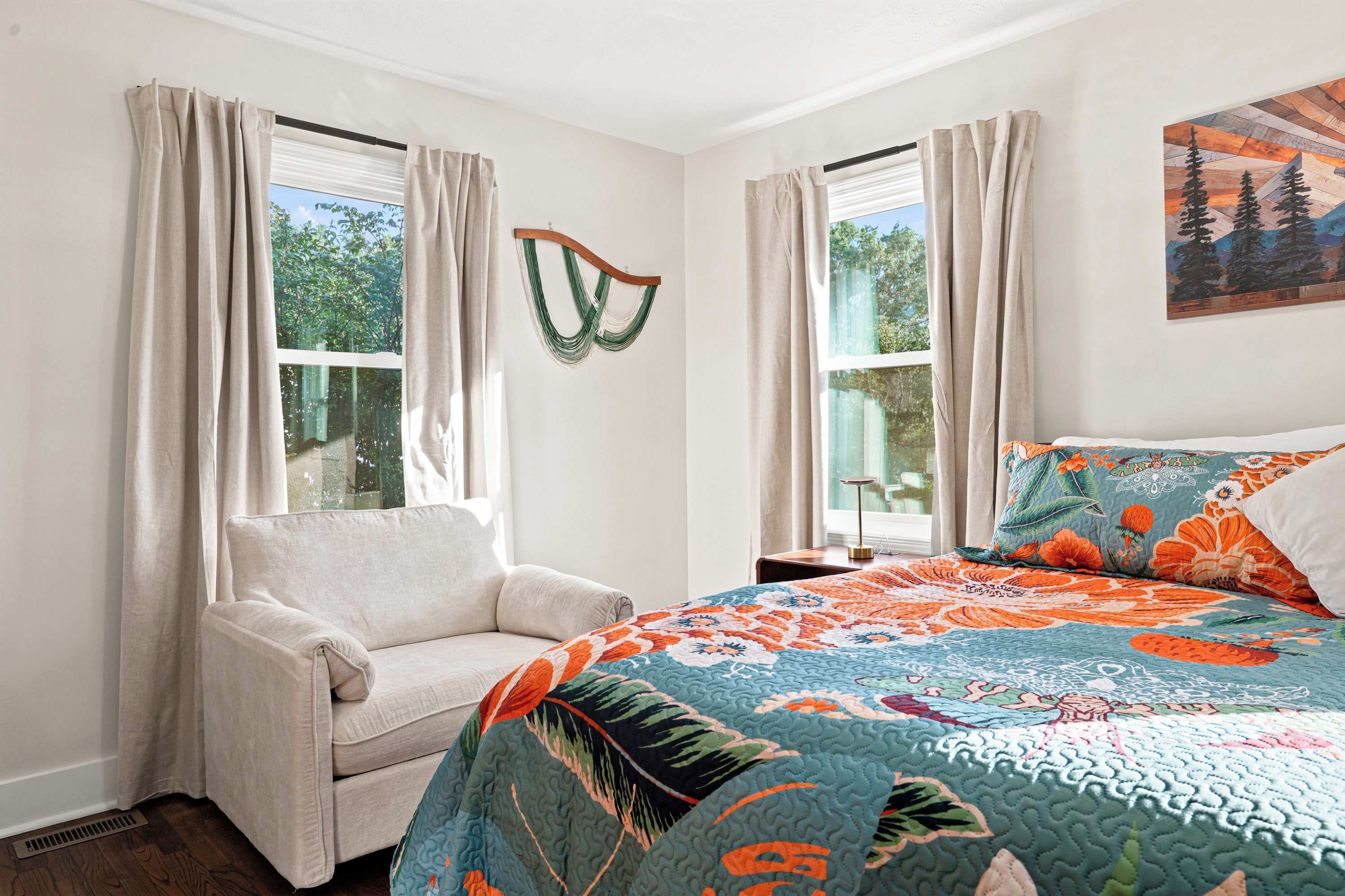 A bedroom with a bed, a chair, and two windows with curtains.