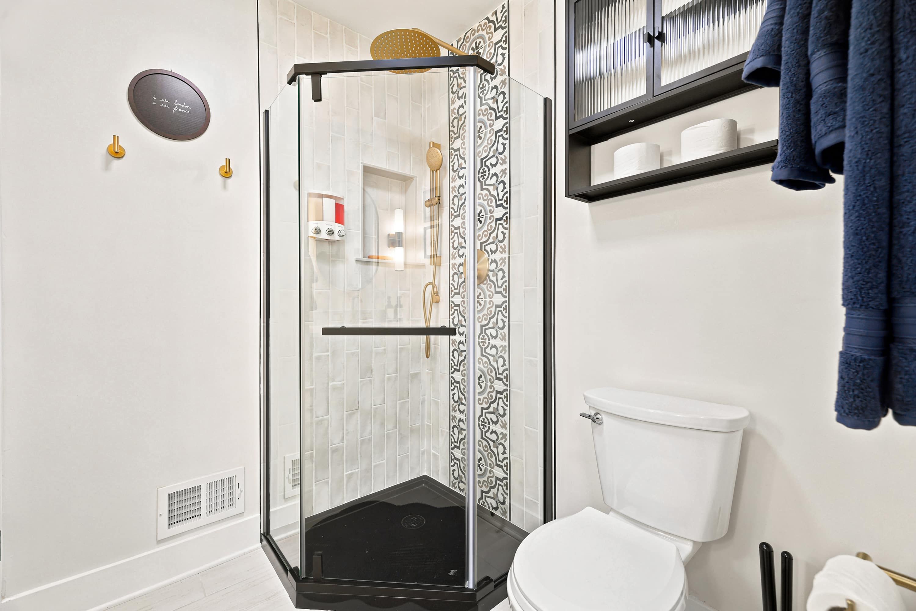 Un baño moderno con ducha envuelta en vidrio, inodoro blanco y un perchero con toallas.