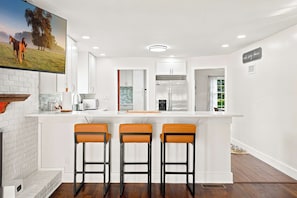 A modern kitchen with white cabinetry, a built-in oven, a refrigerator, and a bar area with three stools.