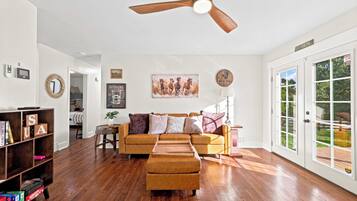 A spacious living room with hardwood flooring, a brown sofa, a coffee table, and a ceiling fan.