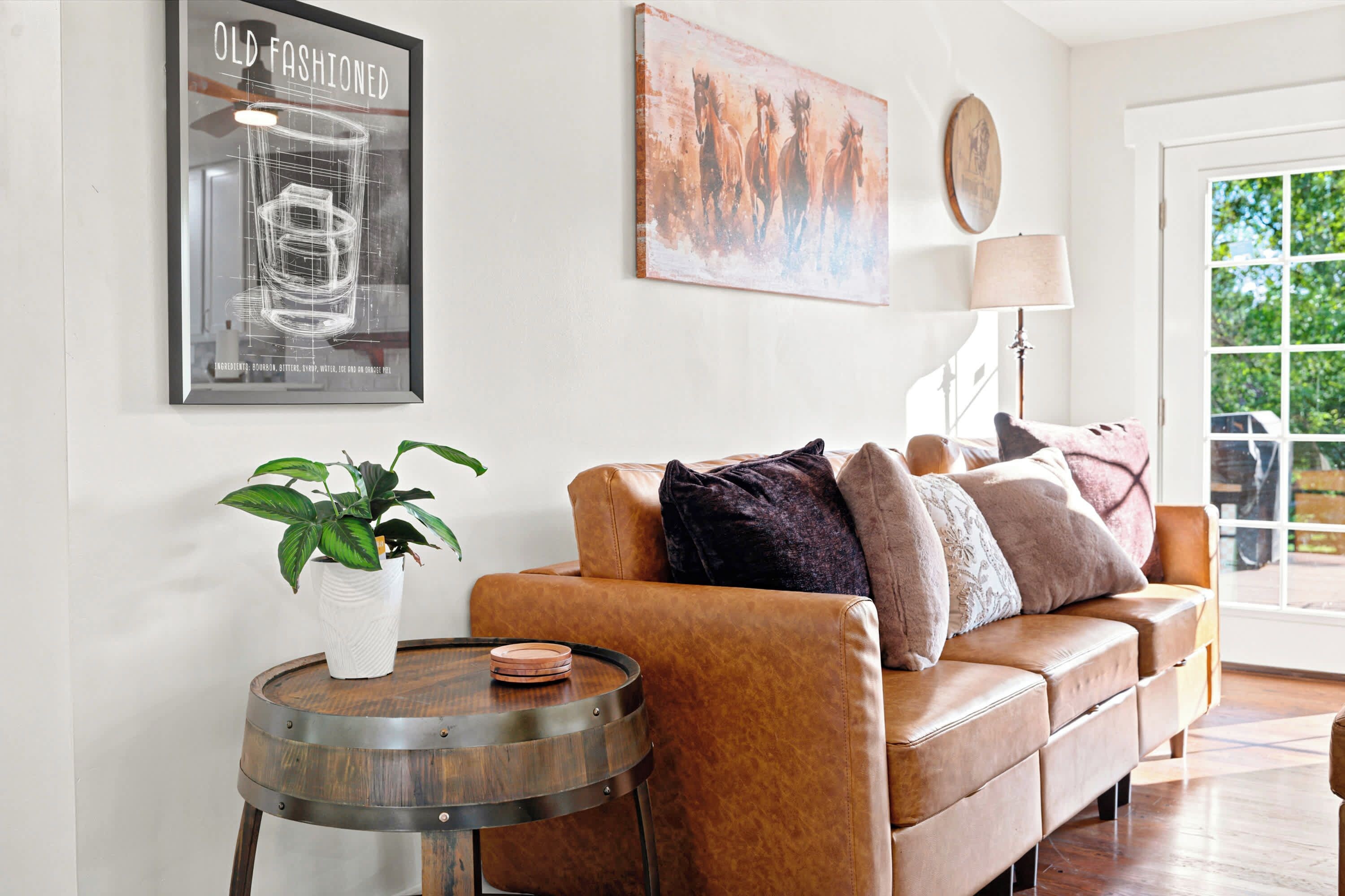 A modern living room with a leather sofa, a round wooden side table, a potted plant, and artwork on the walls.
