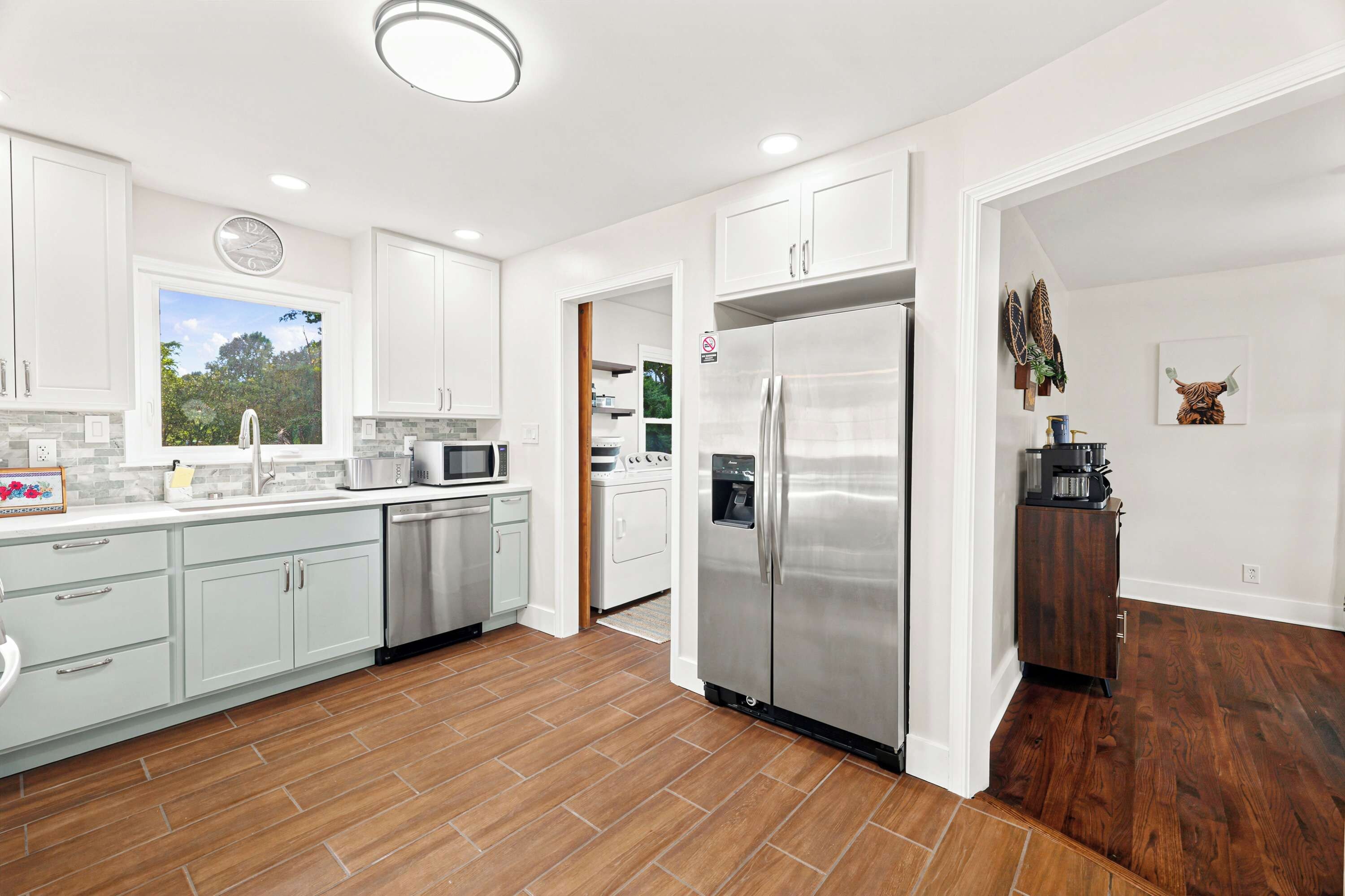 A modern kitchen with white cabinets, stainless steel appliances, and a wooden floor.