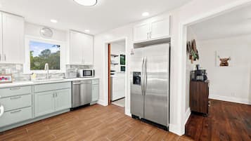 A modern kitchen with white cabinets, stainless steel appliances, and a wooden floor.
