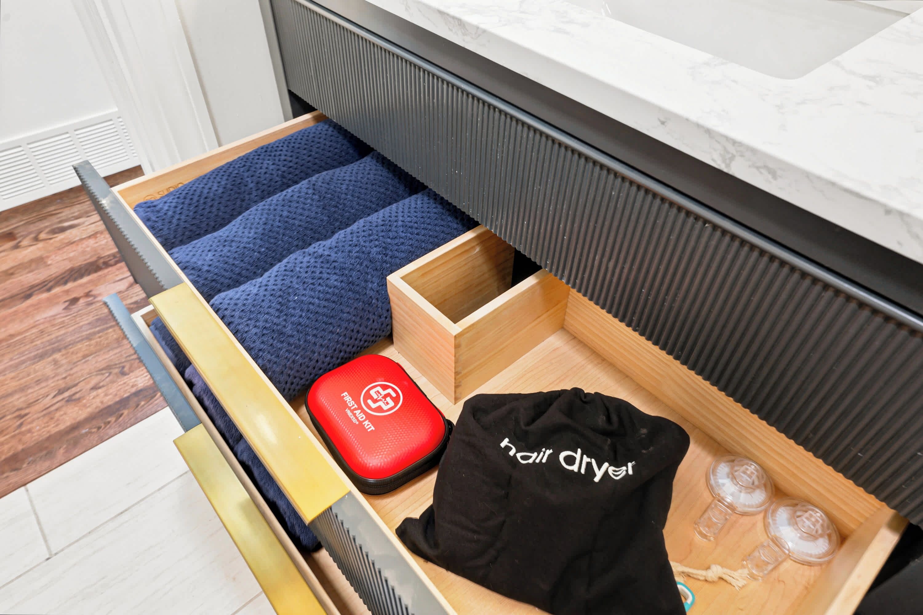 A drawer with a blue towel, a red first aid kit, and a black hair dryer.
