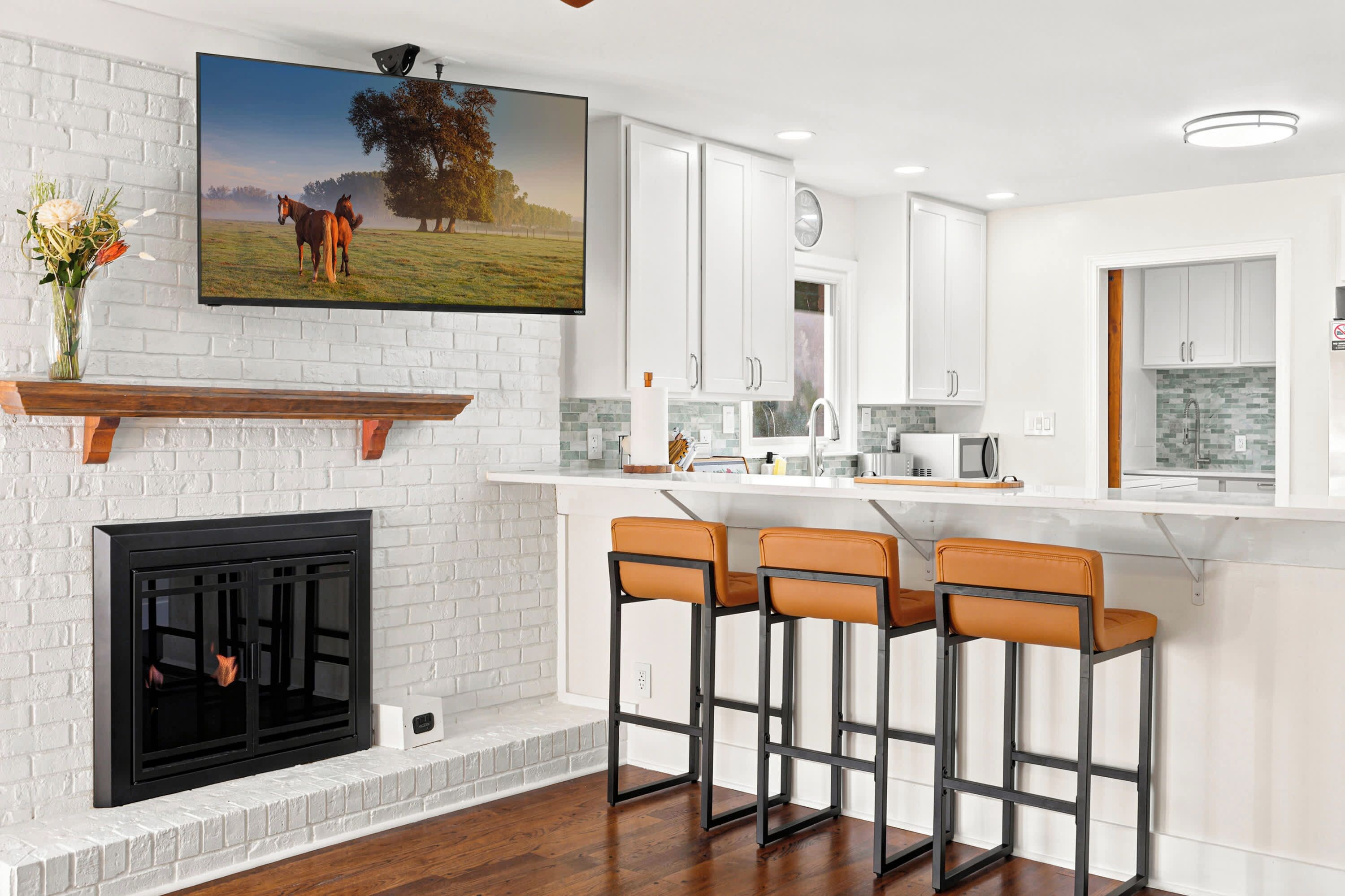 A modern kitchen with white cabinetry, a fireplace, and a bar area with stools.