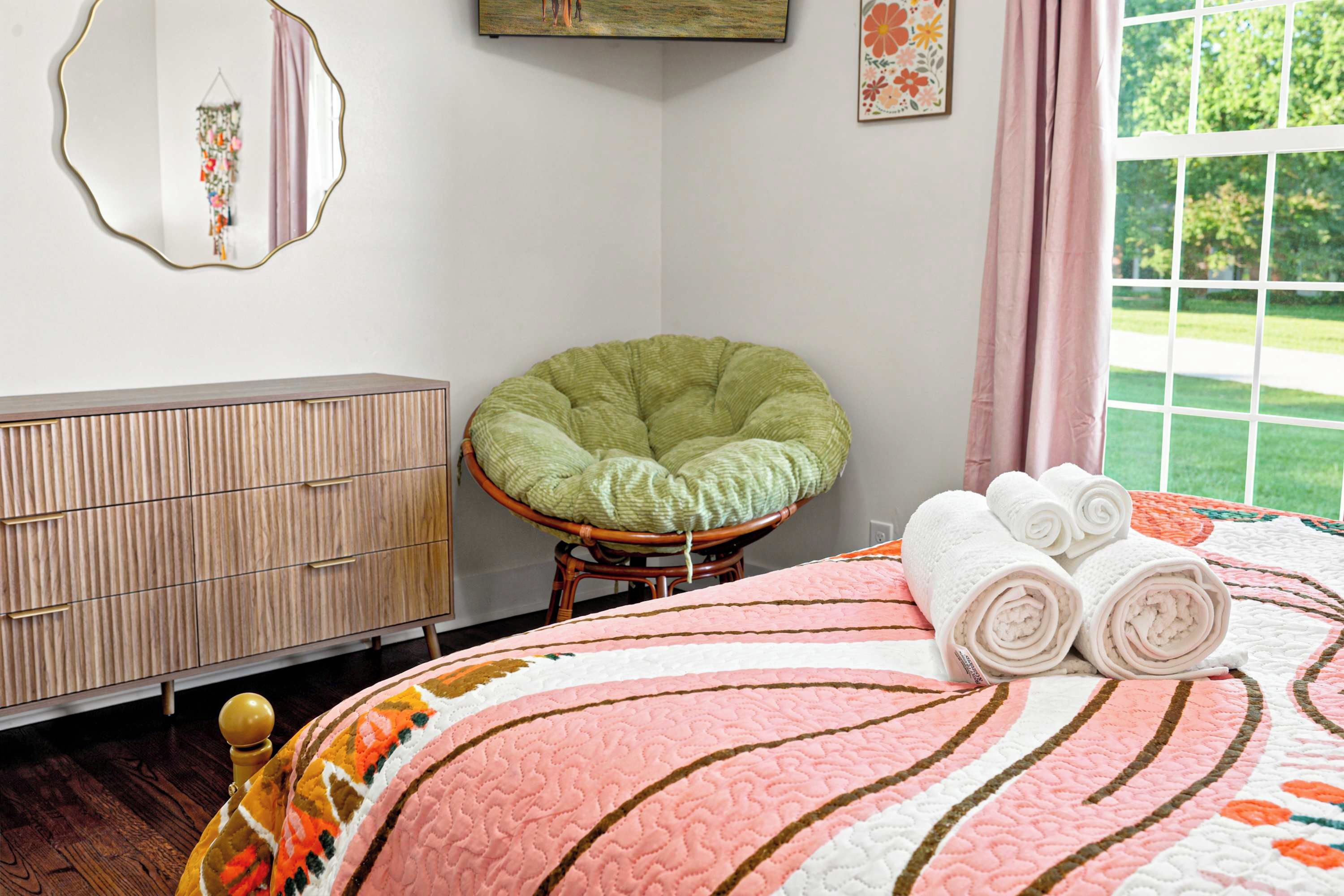 A bedroom with a bed, a chair, a dresser, and a window with a view of greenery.