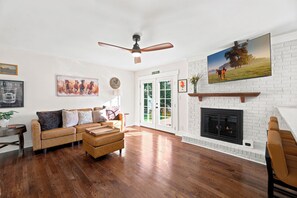 A living room with hardwood flooring, a brown leather sofa, a ceiling fan, and a fireplace.