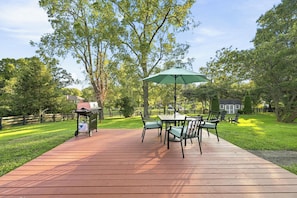 A wooden deck with a table and chairs, a grill, and a green umbrella.