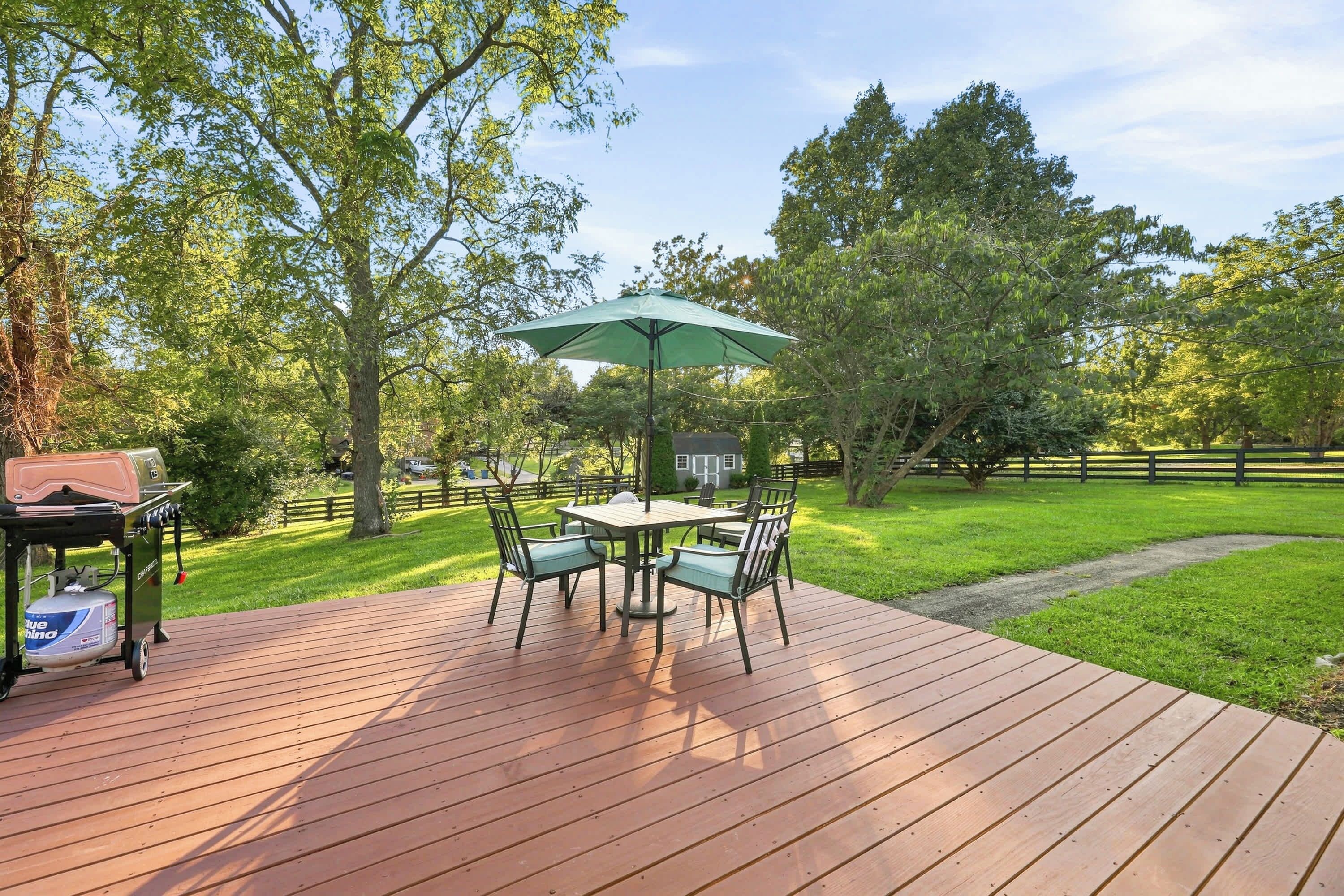 A wooden deck with a table and chairs, a barbecue grill, and a green umbrella.