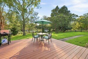 Una terraza de madera con mesa, sillas, una parrilla y un parasol verde.
