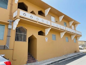 Ein Gebäude mit einer beige farbenen Fassade, einem Balkon mit Verzierungen und einer Treppe, die zu einem Eingang führt.