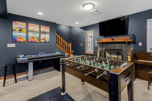 A room with a foosball table, a television mounted on the wall, and a fireplace. - Thanksgiving Open! 6-bedroom, 2 Kitchens, Hot Tub, Game Rm, Piano, Fire Pit,  (Pocono Lake)