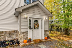 A house with a white front door, stone foundation, and a porch with potted plants and a welcome mat. - Thanksgiving Open! 6-bedroom, 2 Kitchens, Hot Tub, Game Rm, Piano, Fire Pit,  (Pocono Lake)
