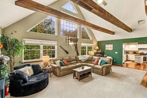 A spacious living area with a high ceiling, large windows, and a kitchen in the background. - Thanksgiving Open! 6-bedroom, 2 Kitchens, Hot Tub, Game Rm, Piano, Fire Pit,  (Pocono Lake)