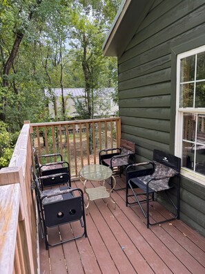 Eine Holzterrasse mit Gartenmöbeln, darunter Stühle und ein Tisch, und Blick auf ein Haus im Hintergrund.