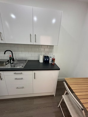 A kitchen with white cabinets, a black countertop, and a wooden bench. - Private Bedroom With Kitchen Access (London)