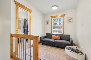 A room with a wooden staircase, a grey sofa, a window with blinds, and a small rug. - Cozy King Condo Walk to Bojangles & Ovens (Charlotte)