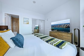A hotel room with a bed, a television, a dresser, and a view of a cityscape.