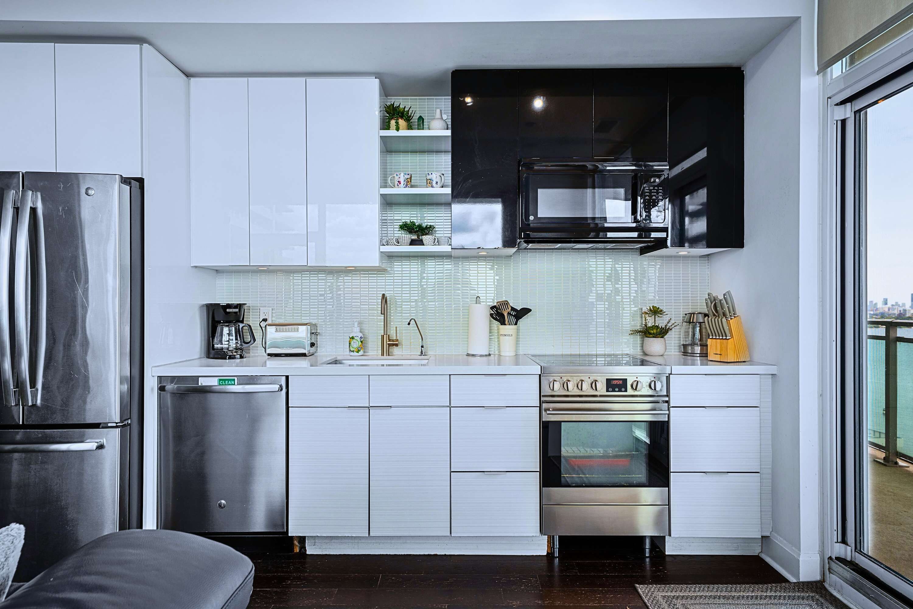 Een moderne keuken met roestvrijstalen apparatuur, witte kasten en een uitzicht op de stad door een groot raam.