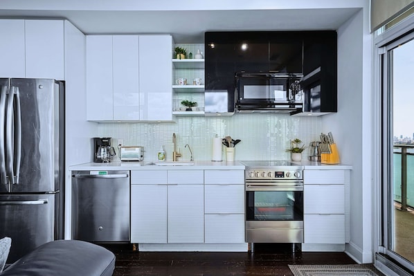 A modern kitchen with stainless steel appliances, white cabinetry, and a view of the city through a large window.