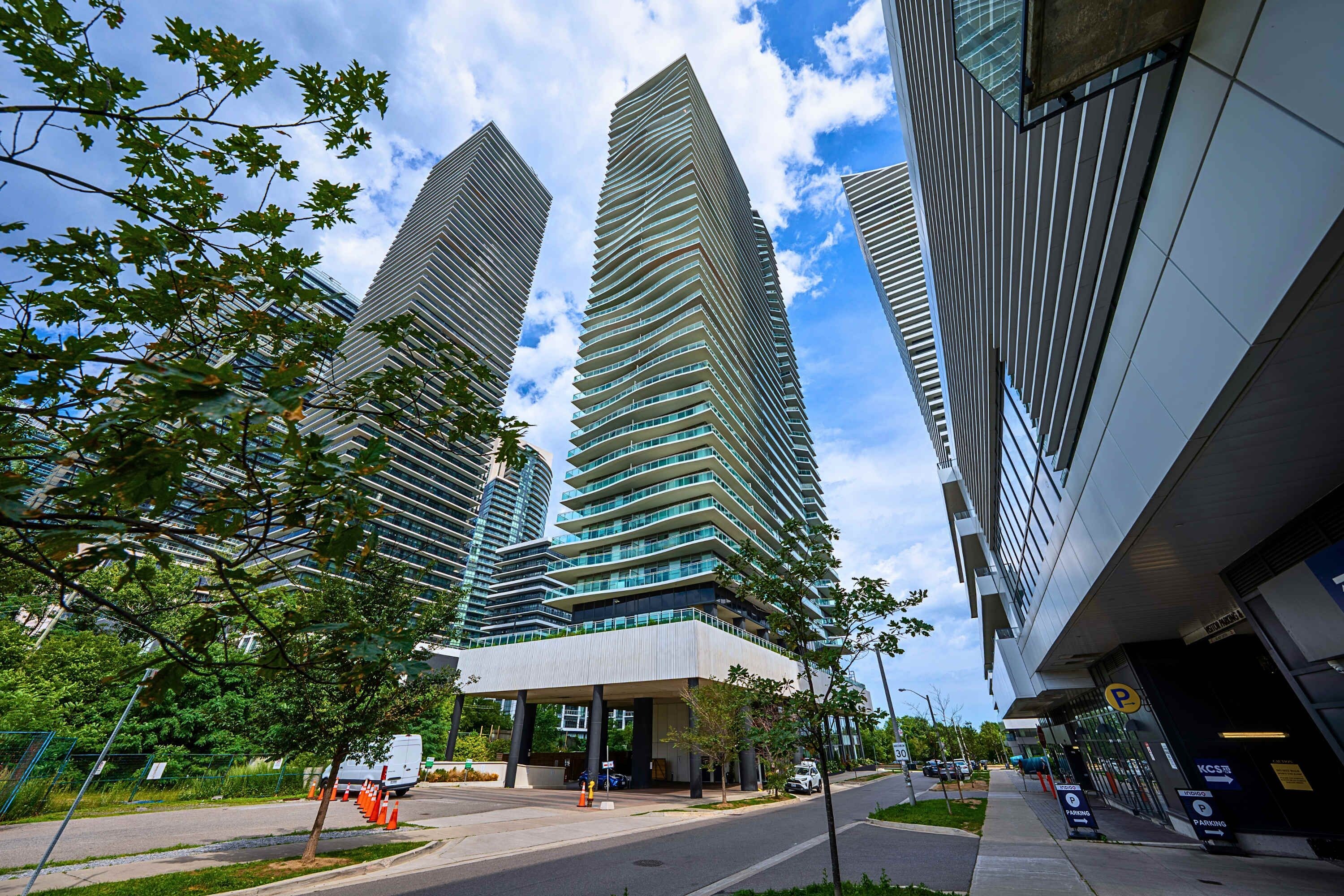 A modern building with a flat roof and multiple floors, surrounded by trees and a parking area.