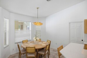 Uma sala de jantar com uma mesa redonda, seis cadeiras, um lustre e uma janela com persianas.