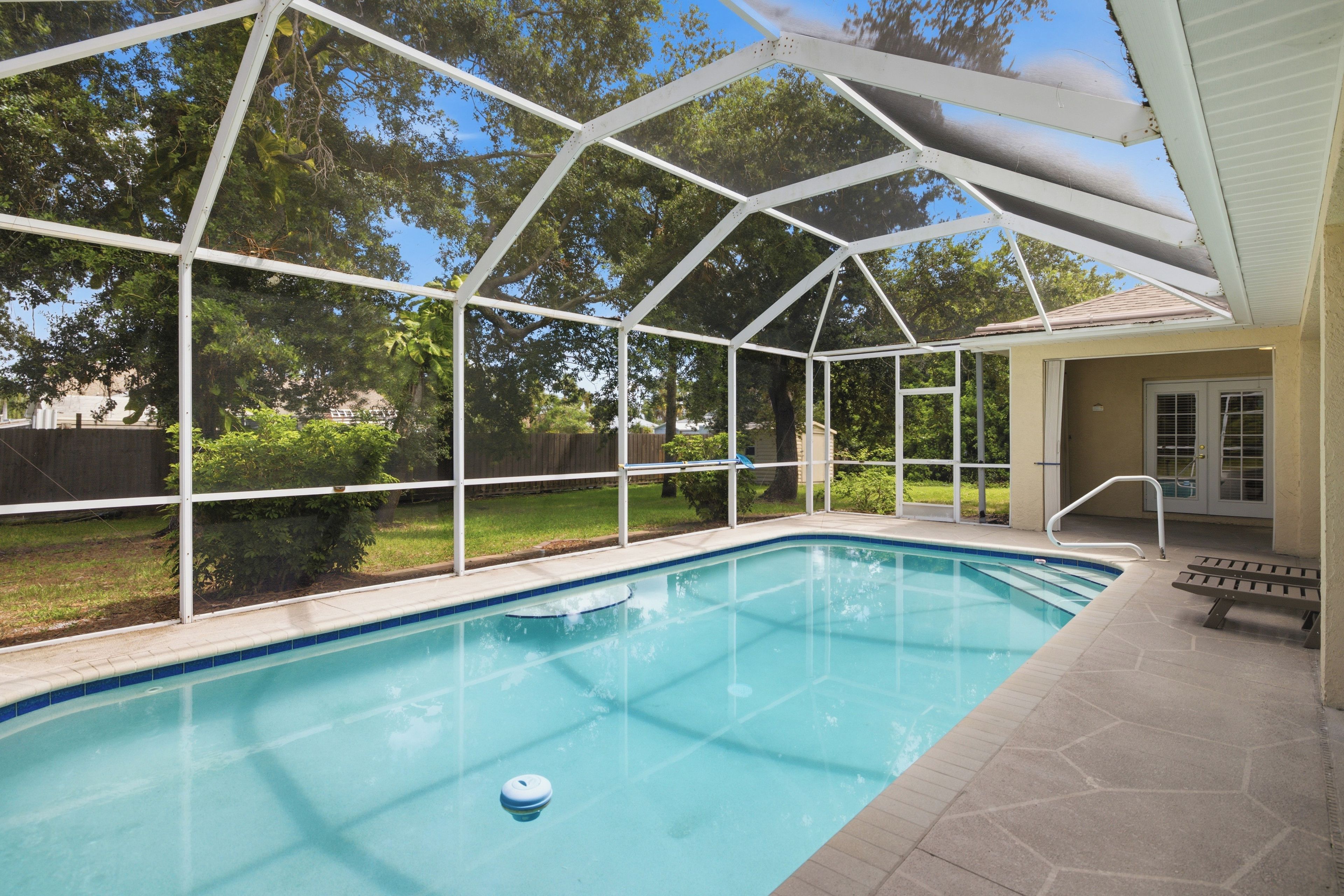 A covered outdoor swimming pool with a clear view of the surrounding area, including a house and trees.