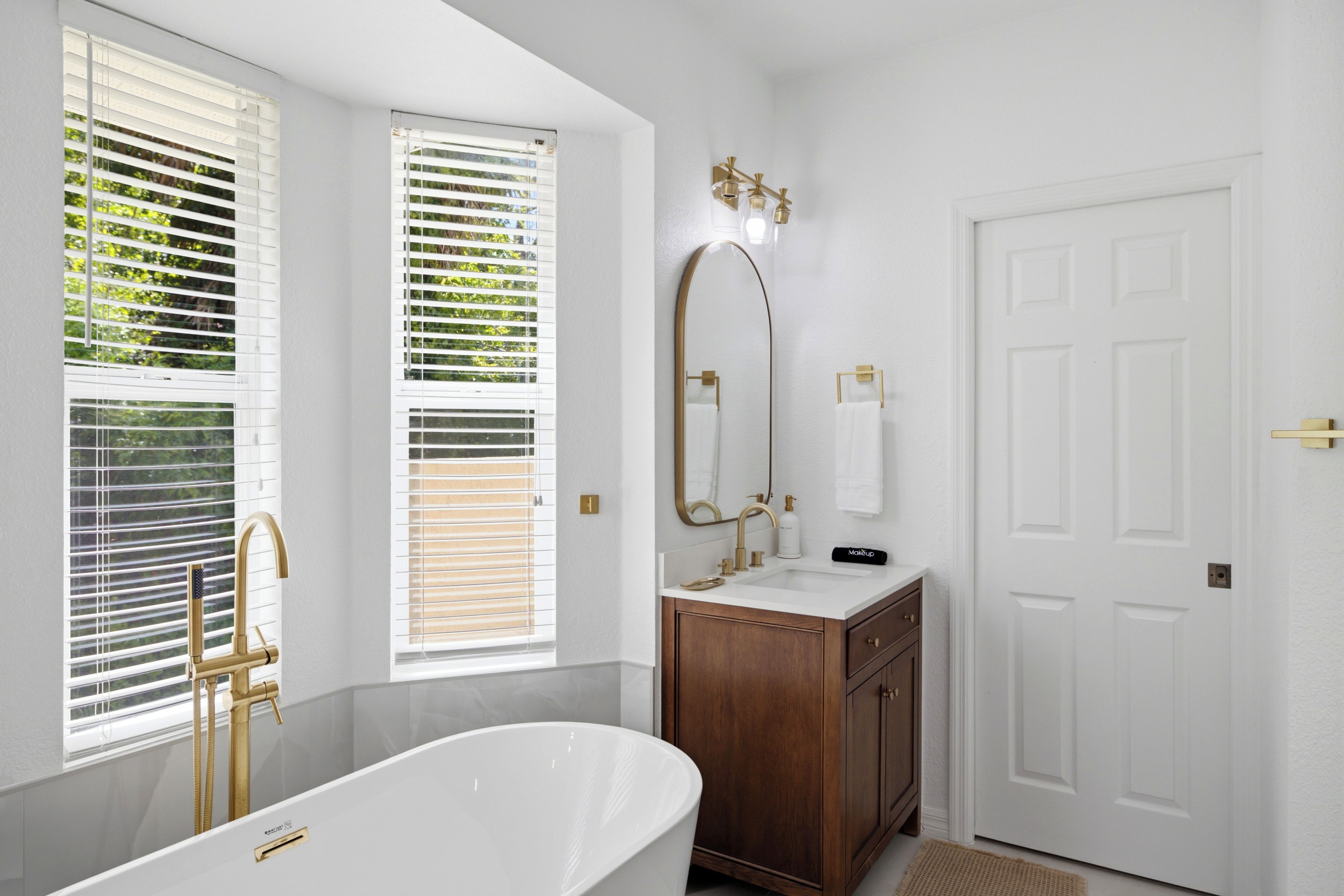 A bathroom with a freestanding bathtub, a vanity with a mirror, and a door.