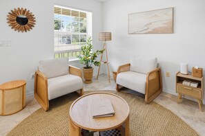 Uma sala de estar com dois poltronas, uma mesa de centro redonda, um abajur, uma planta em vaso e um quadro na parede.
