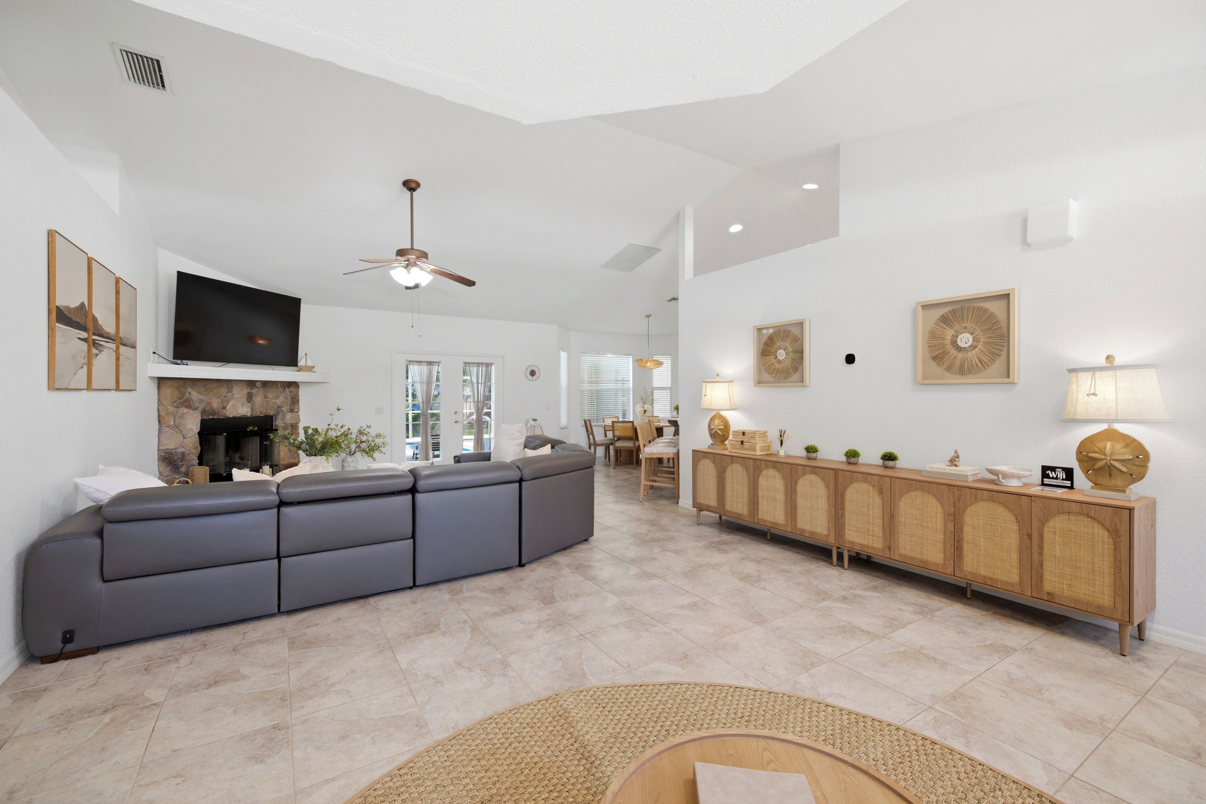 A modern living room with a sectional sofa, a fireplace, a television, and a dining area with a wooden cabinet.
