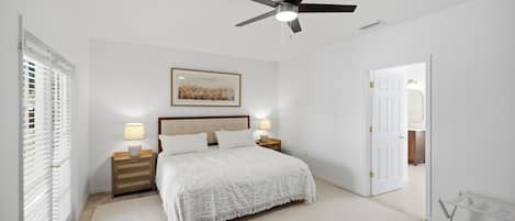 A bedroom with a bed, two bedside tables with lamps, a ceiling fan, a door, and a window with blinds.