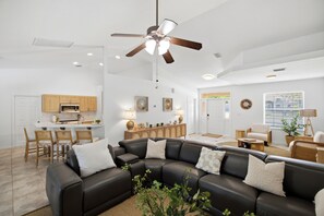 Ein modernes Wohnzimmer mit einer Eckcouch, einem Essbereich mit Holzsäcken und einer Küche mit Mikrowelle.
