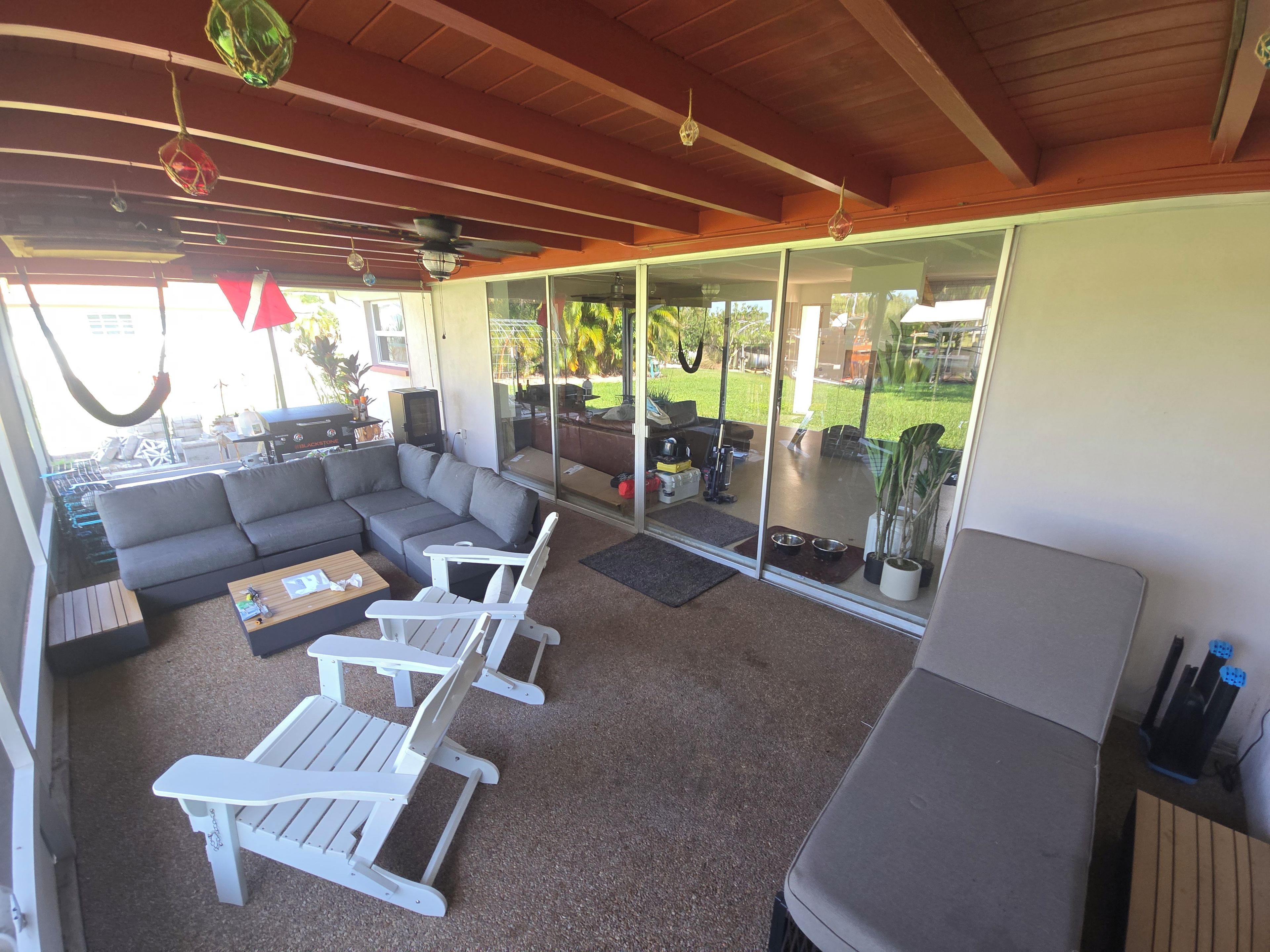 A covered outdoor seating area with a sofa, two white chairs, and a coffee table.
