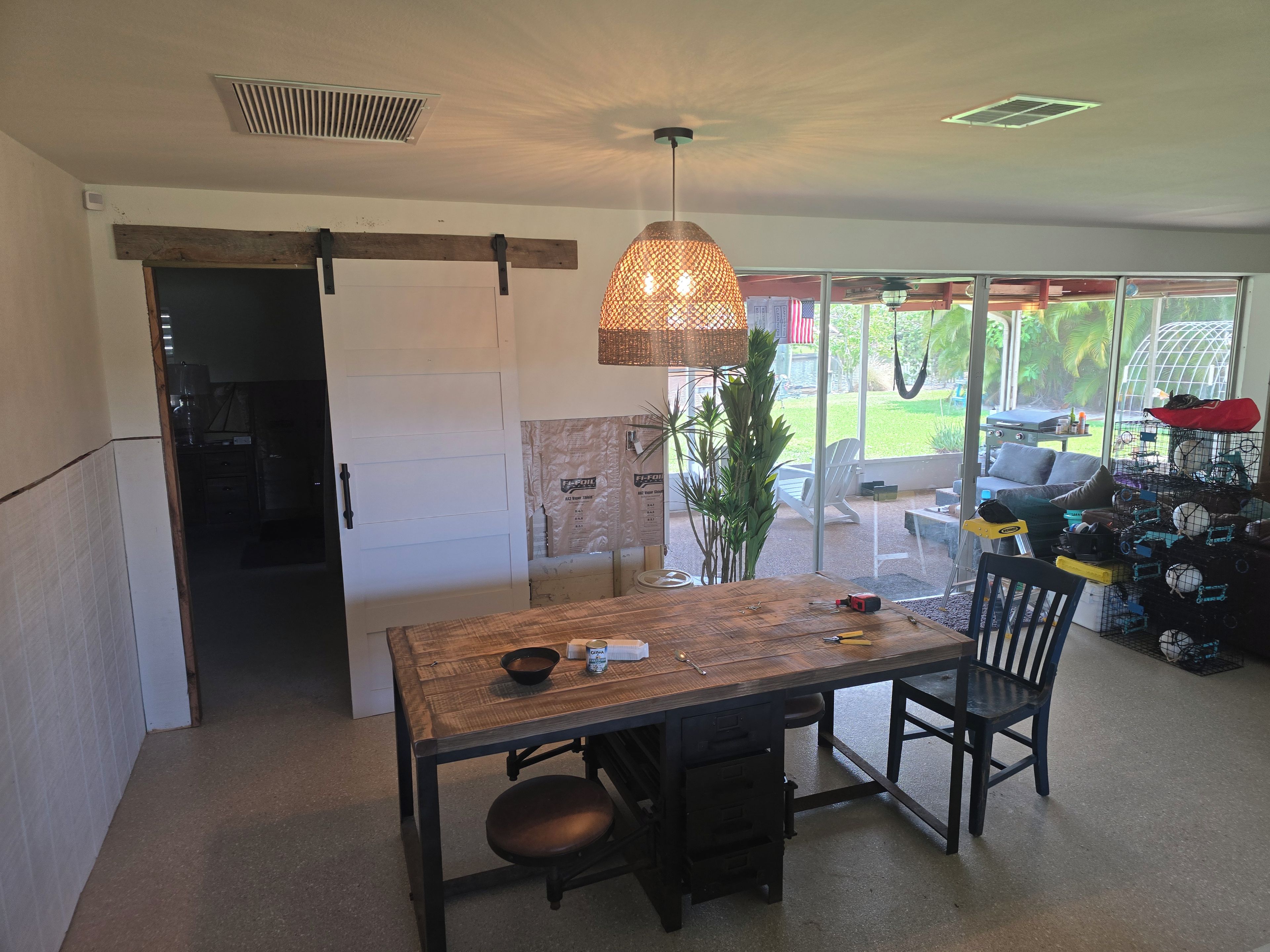 A dining area with a wooden table and chairs, a hanging light fixture, and a view of the outdoors through large windows.
