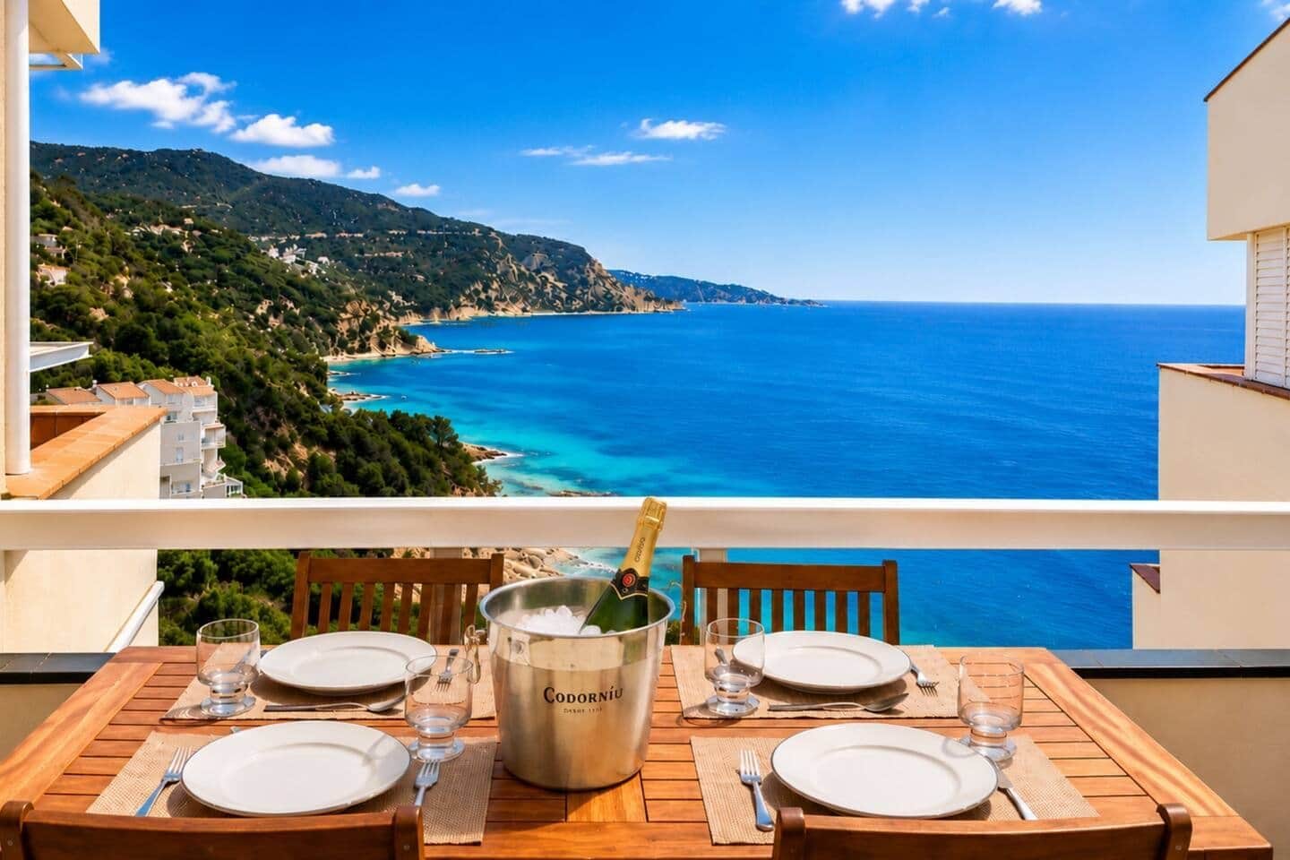 A table set for two with a bottle of champagne, overlooking a coastal landscape.