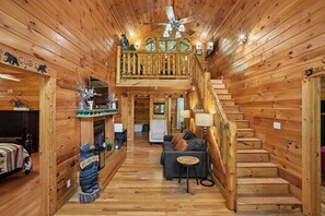A cabin interior with a wooden staircase, a living area with a sofa and a coffee table, and a fireplace. - Private Theater & Hot tub with Arcade and 3 King Beds (Sevierville)