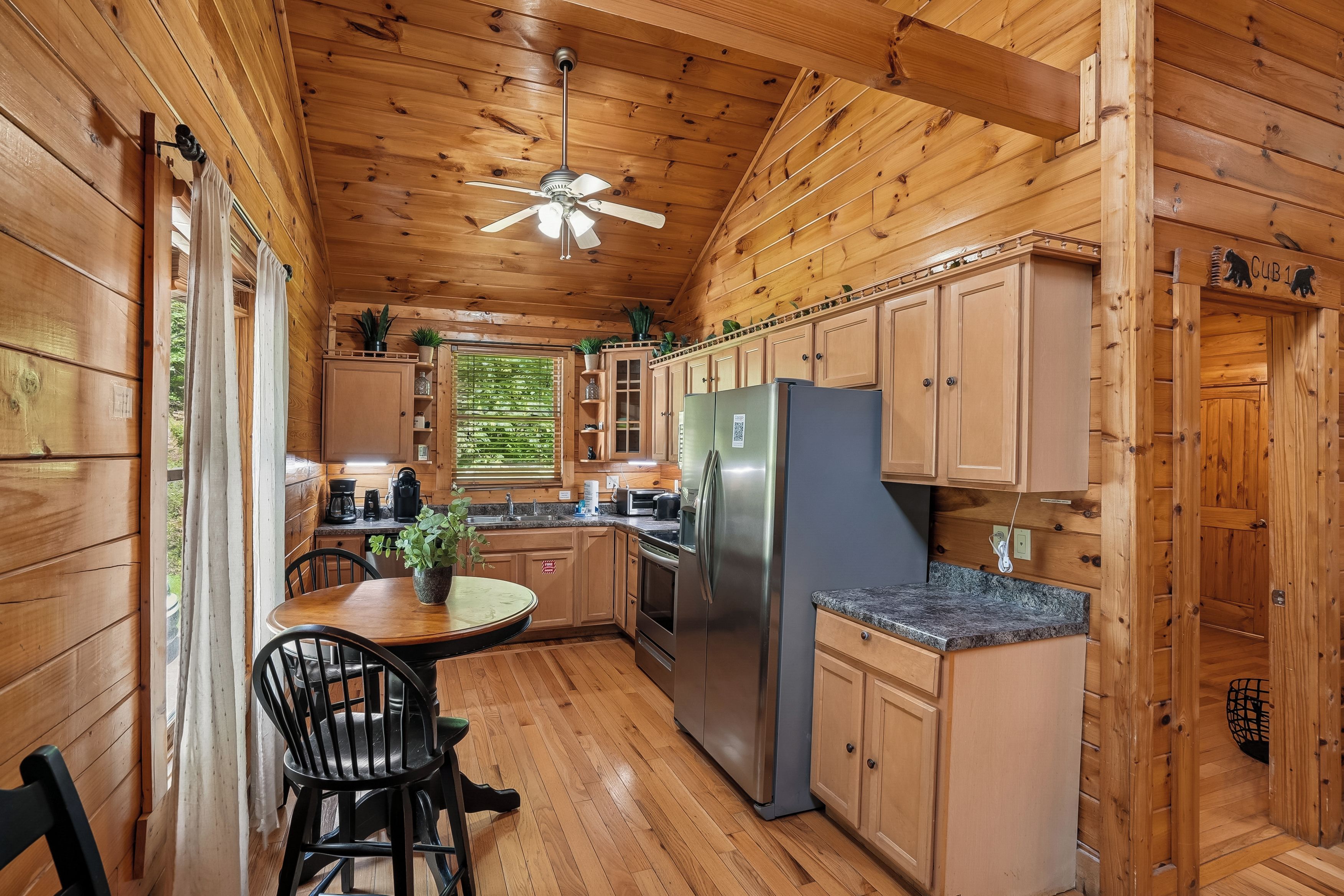 A wooden cabin interior with a kitchen featuring a refrigerator, cabinets, and a dining area with a table and chairs.