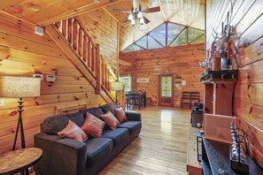 A cozy cabin interior with a wooden staircase, a sofa with cushions, a dining area, and a fireplace. - Private Theater & Hot tub with Arcade and 3 King Beds (Sevierville)