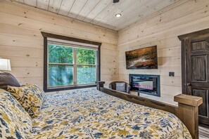 Une chambre à coucher avec un lit, une cheminée, un téléviseur et une fenêtre donnant sur la forêt.