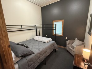A single bed with a headboard, a bedside table with a lamp, and a window with blinds.
