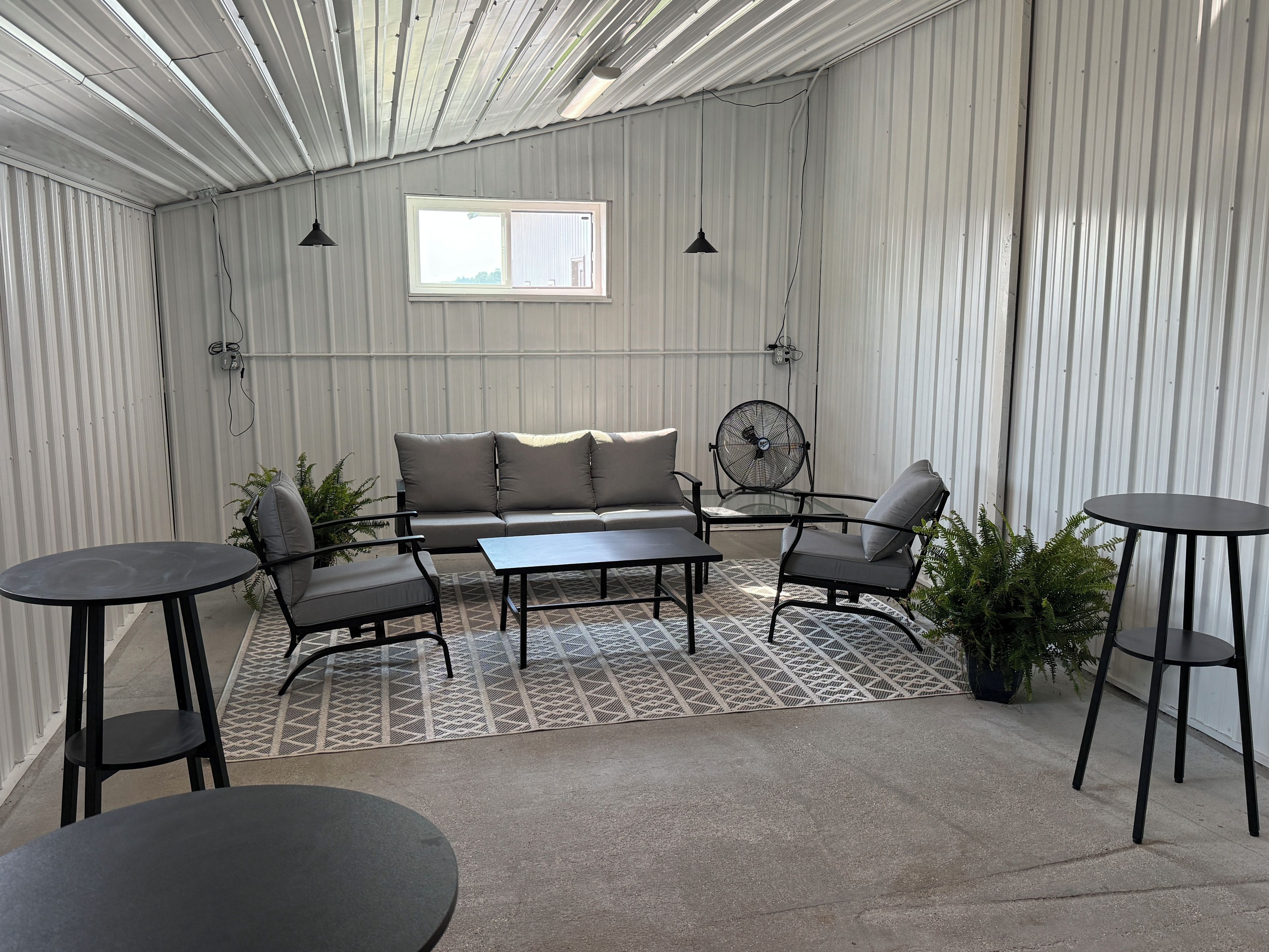 A room with a sofa, two chairs, a table, and a fan.
