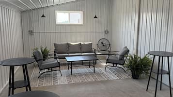 A room with a sofa, two chairs, a table, and a fan.