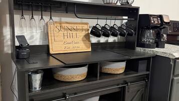 Un comptoir de cuisine avec une machine à café, des verres à vin et une pancarte indiquant « SUNSET HILL, centre d’événements ».