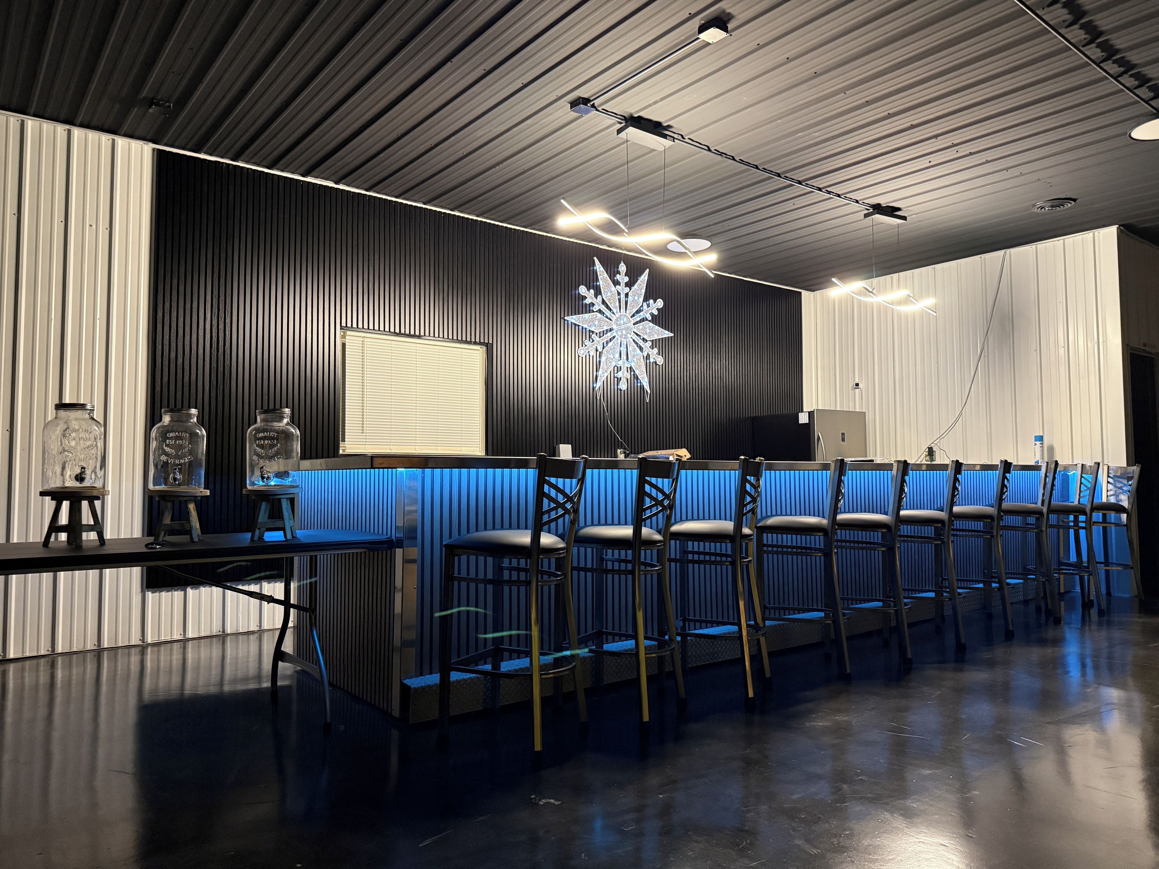 A modern bar area with a long counter, multiple chairs, and a decorative snowflake light fixture.