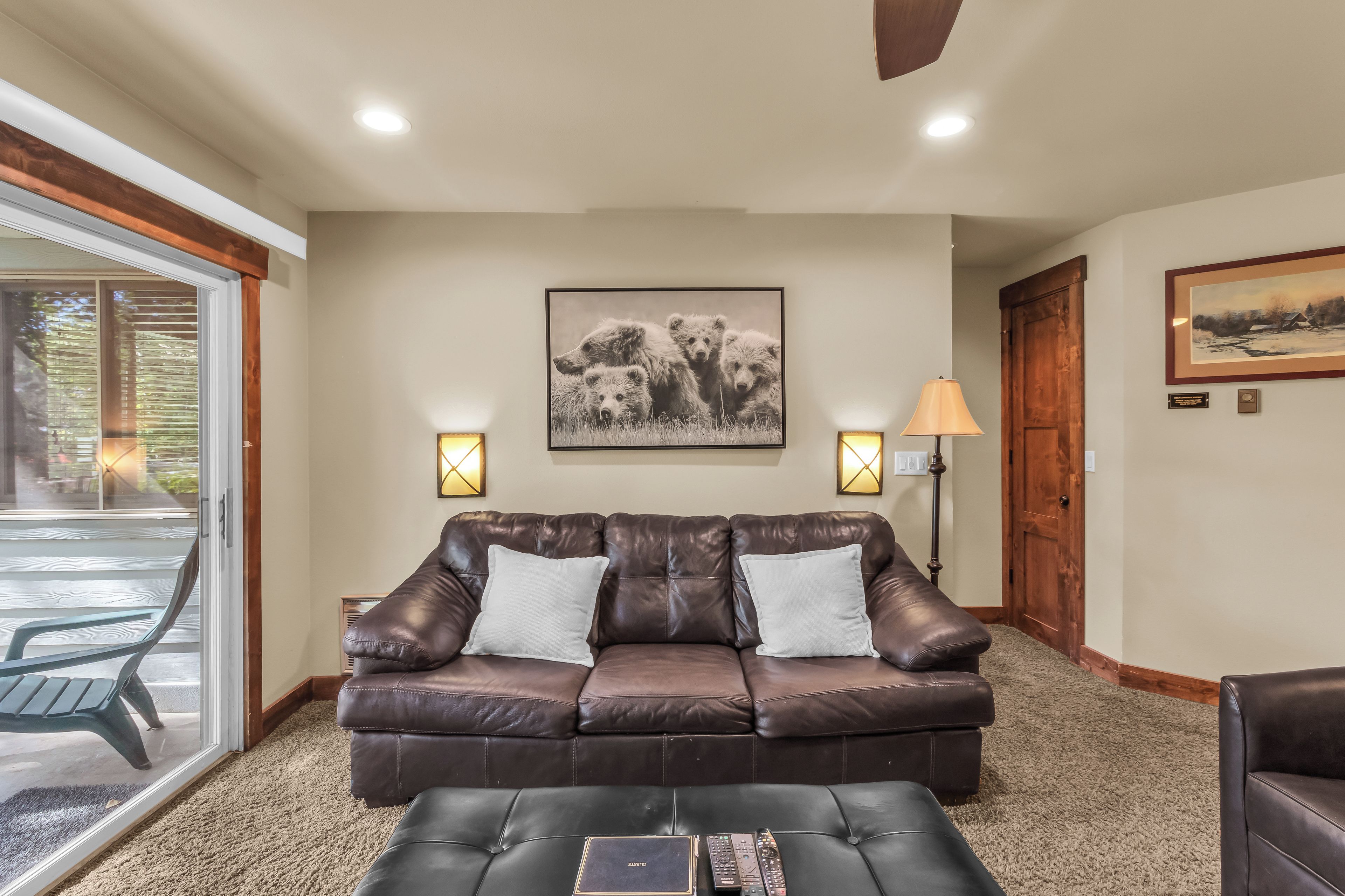 A living room with a brown leather sofa, two white cushions, a coffee table, and a framed picture on the wall.