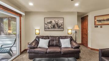 A living room with a brown leather sofa, two white cushions, a coffee table, and a framed picture on the wall.