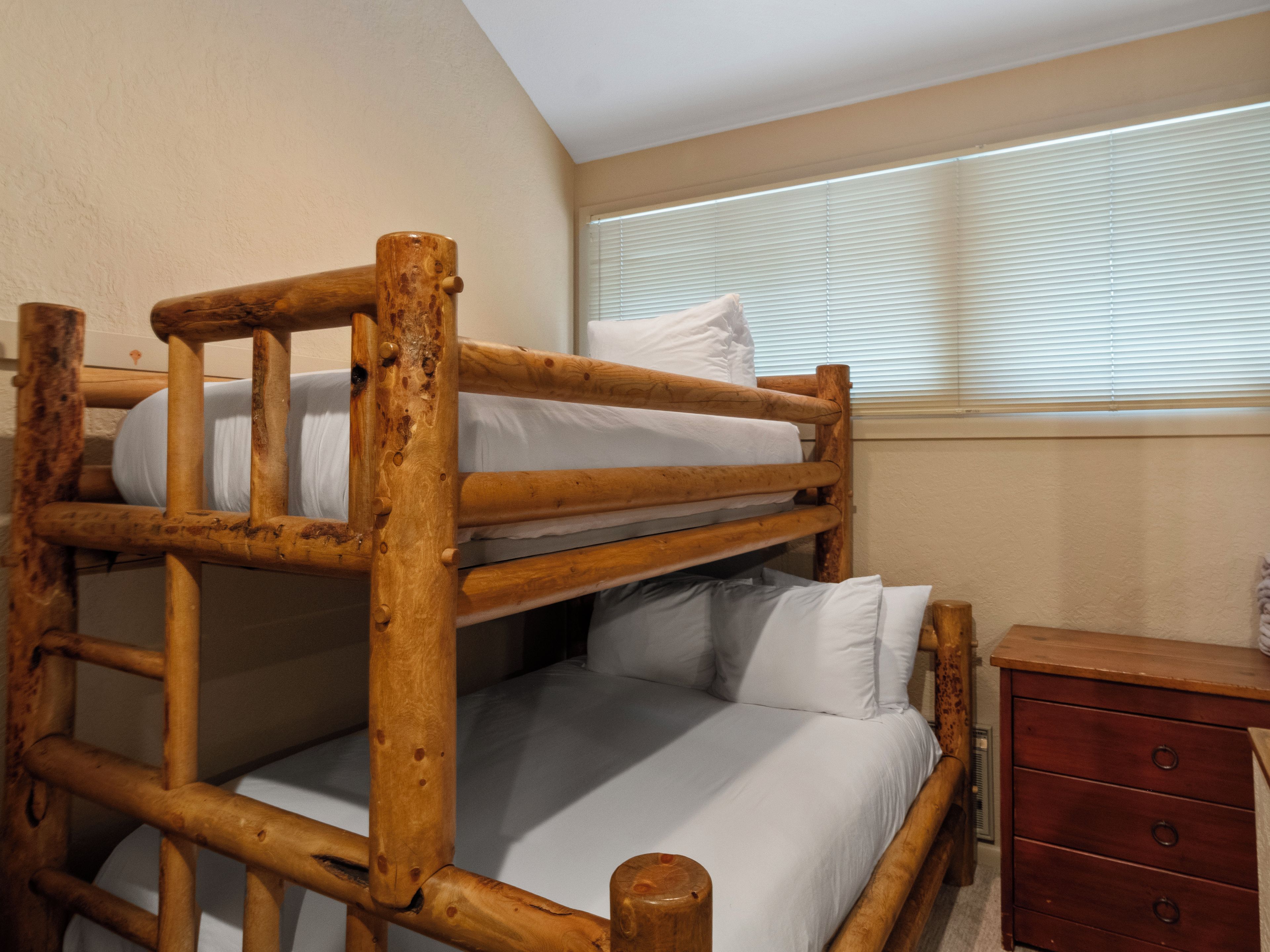 Un lit superposé avec une structure en bois, un lit simple en bas et une petite commode en bois sur le côté droit.