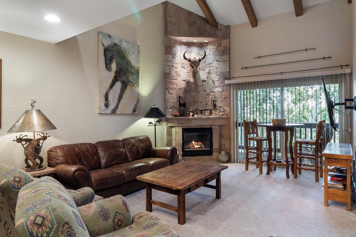 Una sala acogedora con chimenea, sofá de cuero, sillón estampado y un comedor con mobiliario de madera.